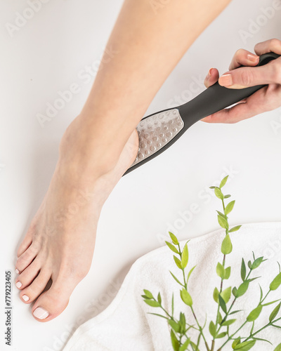 Woman using metal foot file in white modern bathroom