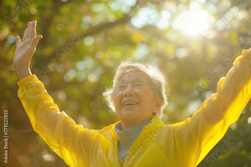 Elderly Asian woman in yellow outfit smiling arms open. Happiness, enjoying life.