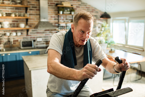 Middle aged man working out on fitness bike at home kitchen photo
