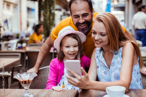 Happy family enjoying time together with smartphone at outdoor cafe