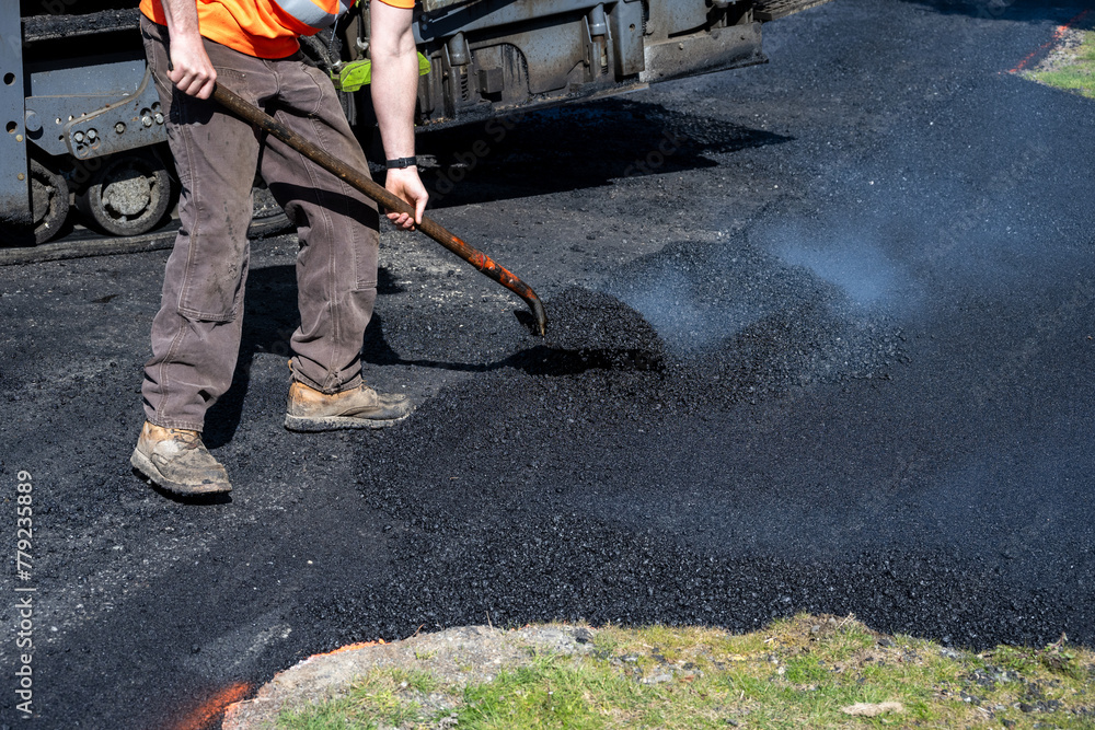 Road crew worker moving hot asphalt with a shovel at the intersection of a driveway and the street, road construction project
Road crew worker moving hot asphalt with a shovel at the intersection of a driveway and the street, road construction project