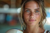 A captivating young woman with blue eyes and freckles holding a volleyball, exuding confidence and spirit