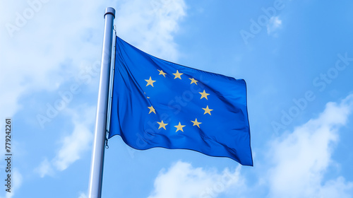 European Union Flag waving in the wind on flagpole over a blue and cloudy sky 