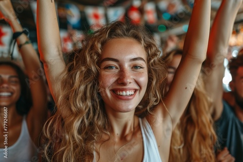 Joyful woman with curly hair and freckles smiling and celebrating at a crowded event with hands raised