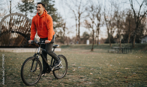 Cheerful young man enjoys a bike ride in a serene park setting as the evening light softens.