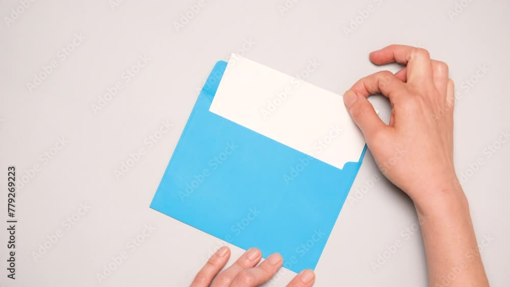A hand pulls out a white card from a bright blue envelope. Top view of a blue envelope on gray background. Banner for social media ad with copy space. A hand pulls out a white card from a bright blue envelope. Top view of a blue envelope on gray background. Banner for social media ad with copy space.