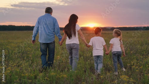 Happy family walks holding hands in park sunset. Children, parents relax carefree. Family walks on green grass with flowers. Family travel parents daughter son. People traveling outdoor. Happy people