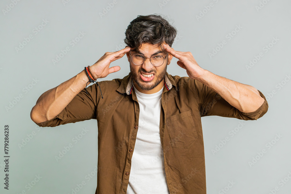 Displeased exhausted Indian Hindu man guy rubbing temples to cure headache problem, suffering from tension, migraine, stress, grimacing in pain, high blood pressure isolated alone on gray background Displeased exhausted Indian Hindu man guy rubbing temples to cure headache problem, suffering from tension, migraine, stress, grimacing in pain, high blood pressure isolated alone on gray background
