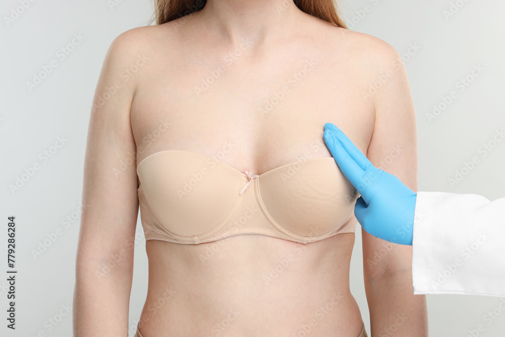 Mammologist checking woman's breast on light grey background, closeup