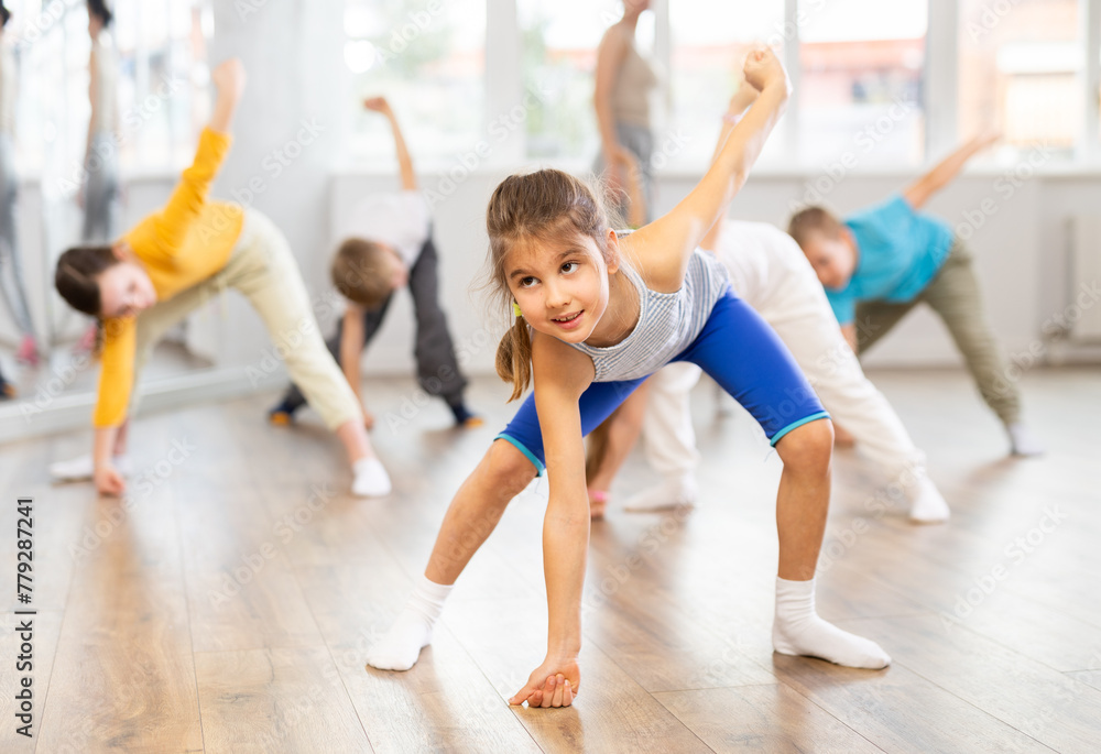 Group of focused tween children standing akimbo in row one by one, learning movements of folk dance in choreography lesson