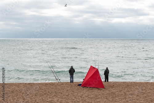 Men fishing on the beach with red tent on the foreground