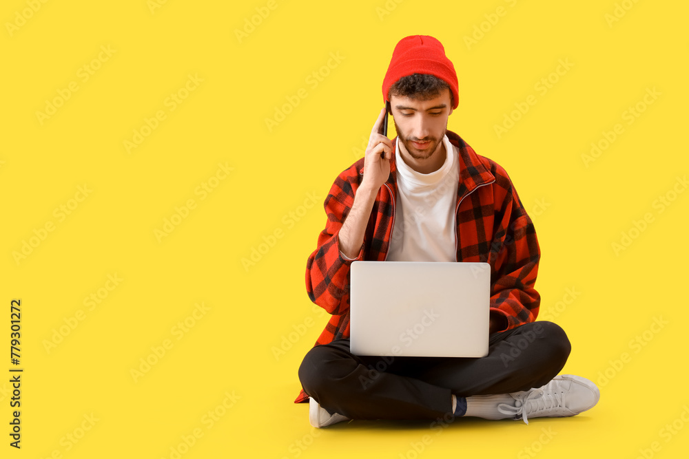 Handsome young man with laptop talking by mobile phone on yellow background Handsome young man with laptop talking by mobile phone on yellow background