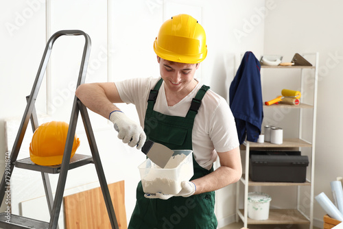 Male decorator with putty knife and plaster working in room