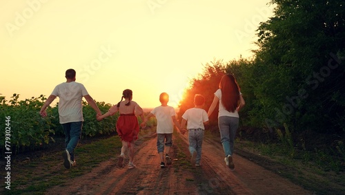 Dad mom, daughter, son run hand in hand, family team. Parents and kids, Dad, Mom, children run in summer at rural sunset. Large family walks through field of sunflowers, group of people runs in nature
