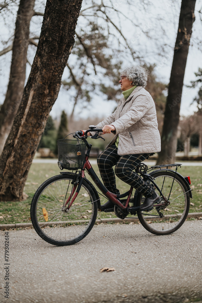 Mature woman cyclist with gray hair wearing a warm jacket, experiencing the joy of active retirement as she rides her bicycle in the park.