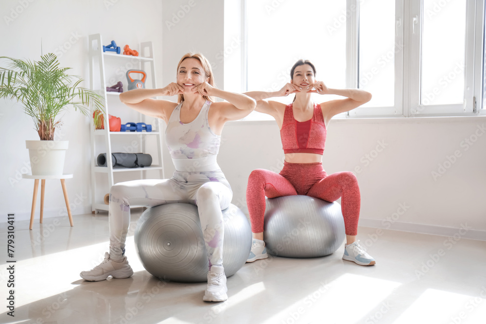 Obraz premium Beautiful happy mature woman with physiotherapist doing face building exercise on fitballs in rehabilitation center