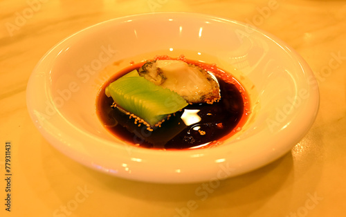 fresh abalone with green lettuce in red spicy oil in the white plate