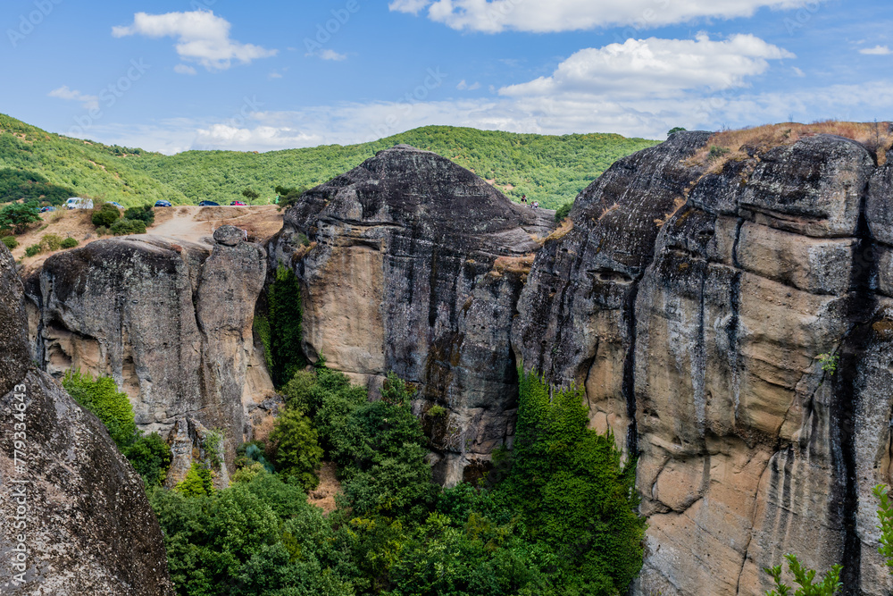 Dramatic rock formations with intricate patterns and dense greenery at their base in Meteora, Greece