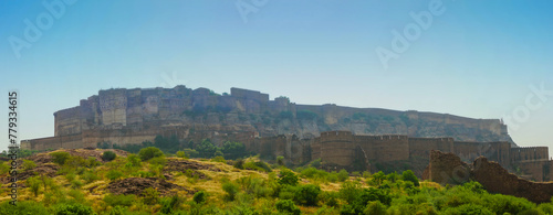 Panoramic view of Mehrangarh fort from Rao Jodha desert rock park, Jodhpur, India. Green vegetation in the foreground and Mehrangarh fort in the background, with rocky landscape of the desert park.