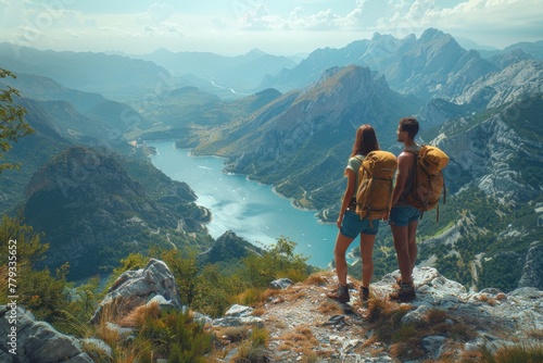 A couple stands captivated by the serene view of a winding lake from a high mountain trail.