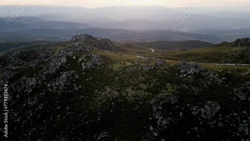 Dark moody light scross exposed rocks poking out above green hillside with winding road,Sierra de san mamede Ourense Spain photo