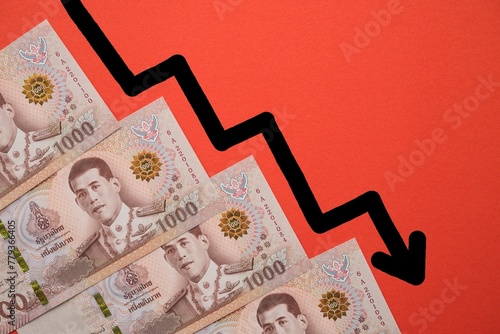 Thai thousand 1000 Baht banknotes and falling down chart graph on red background with copy space. Thailand or Asia business, economy, financial and investment concept.