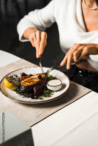 A woman eats a salmon steak in a restaurant.Fish meat cooked on a plate.Food concept