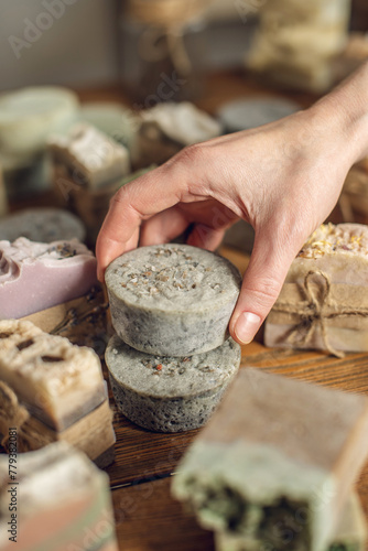 A lot of pieces of fragrant  beautiful natural soap on a wooden table in the workshop and the hand of a woman soap maker carefully takes one piece