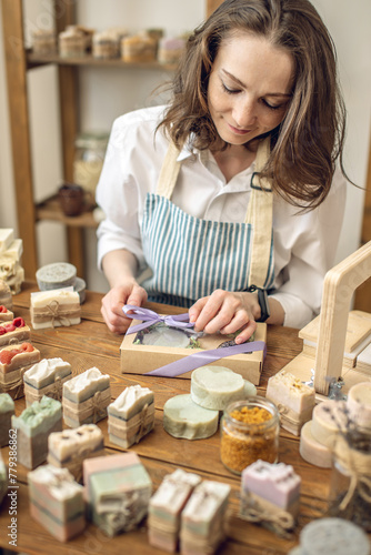 Woman soap maker in a workshop is packing in the gift box handmade natural soap. Cozy creative atmosphere and nice hobby