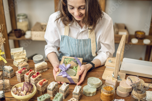 Woman soap maker in a workshop is packing in the gift box handmade natural soap. Cozy creative atmosphere and nice hobby