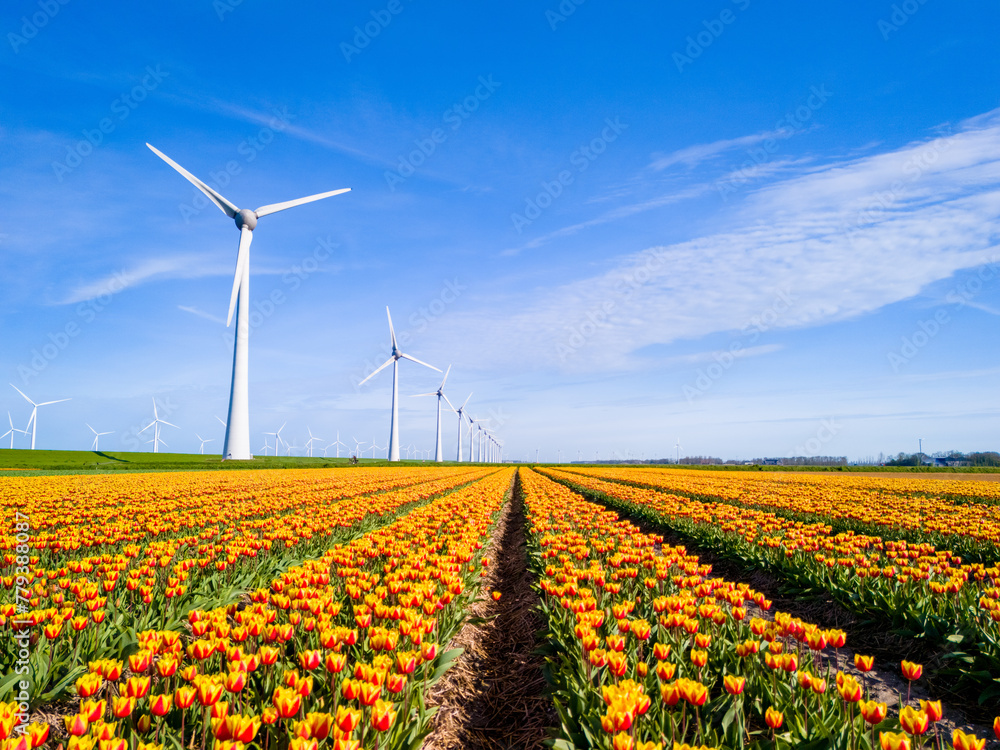 A vast field of colorful flowers sways gracefully in the wind, with towering windmills in the background