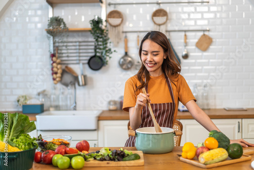 Young woman standing near stove and cooking  housewife  meal  chef  food.Happy woman looking and smelling tasting fresh delicious from soup in a pot with steam at white interior kitchen