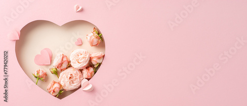 Sophisticated Mother's Day display: Top view of roses, and paper hearts in a heart-shaped frame on soft pink surface, with text space for greetings or ads