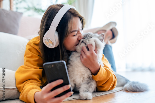 Spending your free time at home with your cat. young asian woman in headphones, with mobile phone, lies on floor in living room, with fluffy Maine Coon cat, listens to music