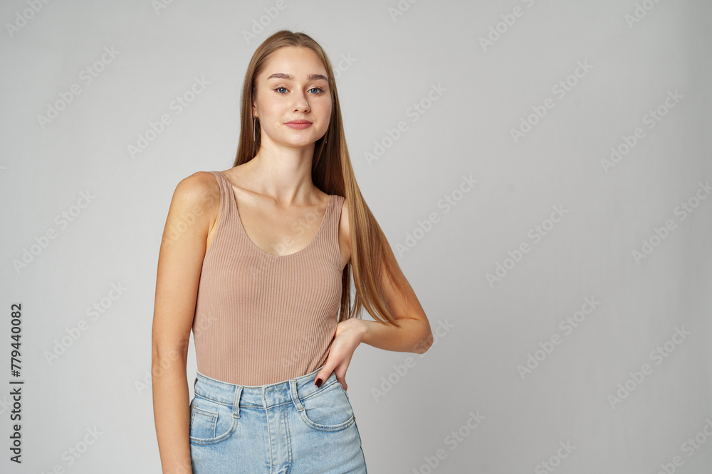 Young Woman Wearing High Rise Jeans and Tank Top posing on gray background in studio Young Woman Wearing High Rise Jeans and Tank Top posing on gray background in studio