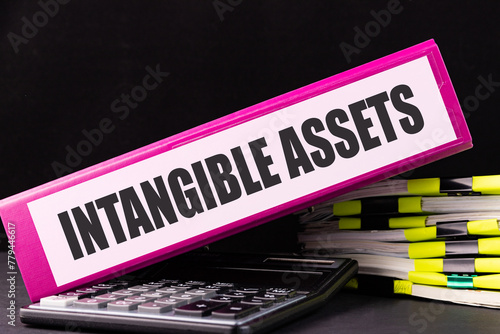 INTANGIBLE ASSETS text is written on a folder lying on a stack of papers on an office desk. Business concept. photo