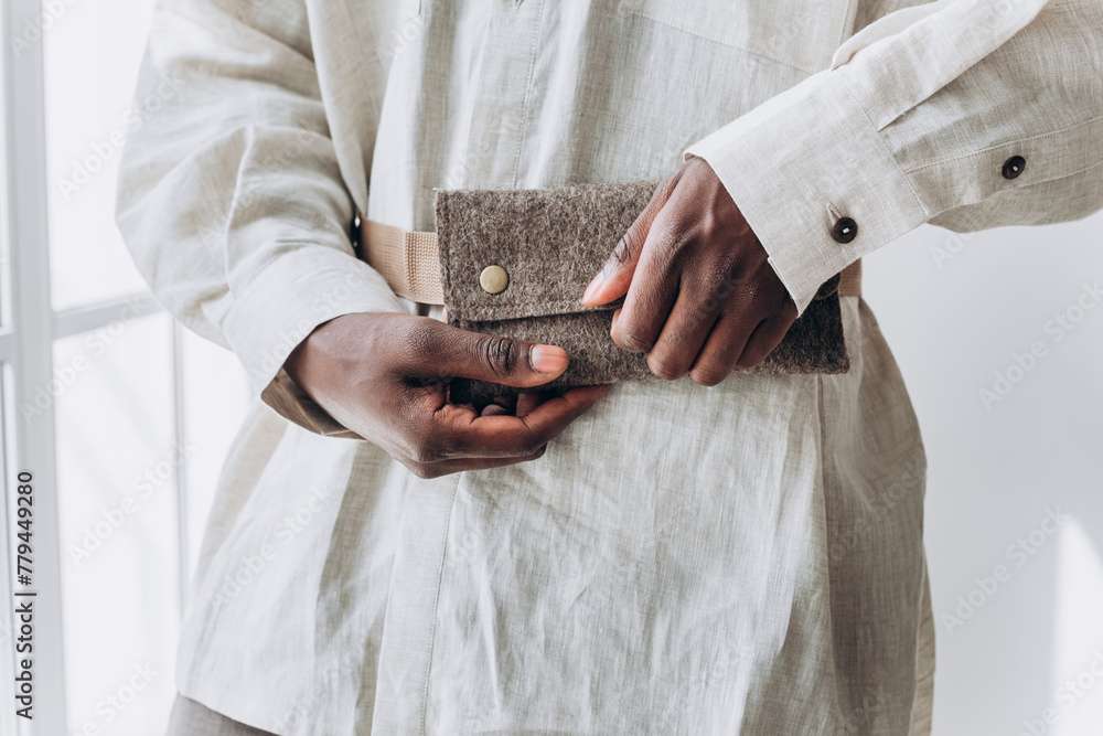 Close-Up of African American Man's Hands Holding a Textured Wallet. Close-up of a person's hands fastening a stylish felt wallet, showcasing a blend of practicality and fashion in soft natural - obrazy, fototapety, plakaty 