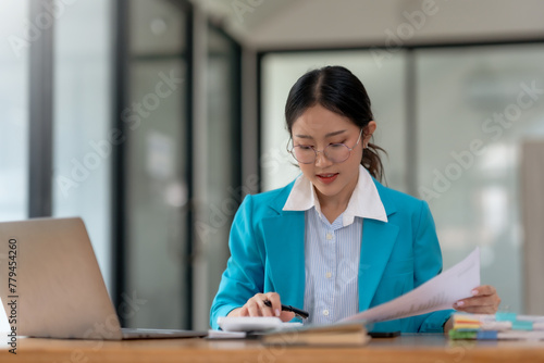 Young Asian businesswoman using a calculator to calculate business principles. Accounting statistics concept at the office.