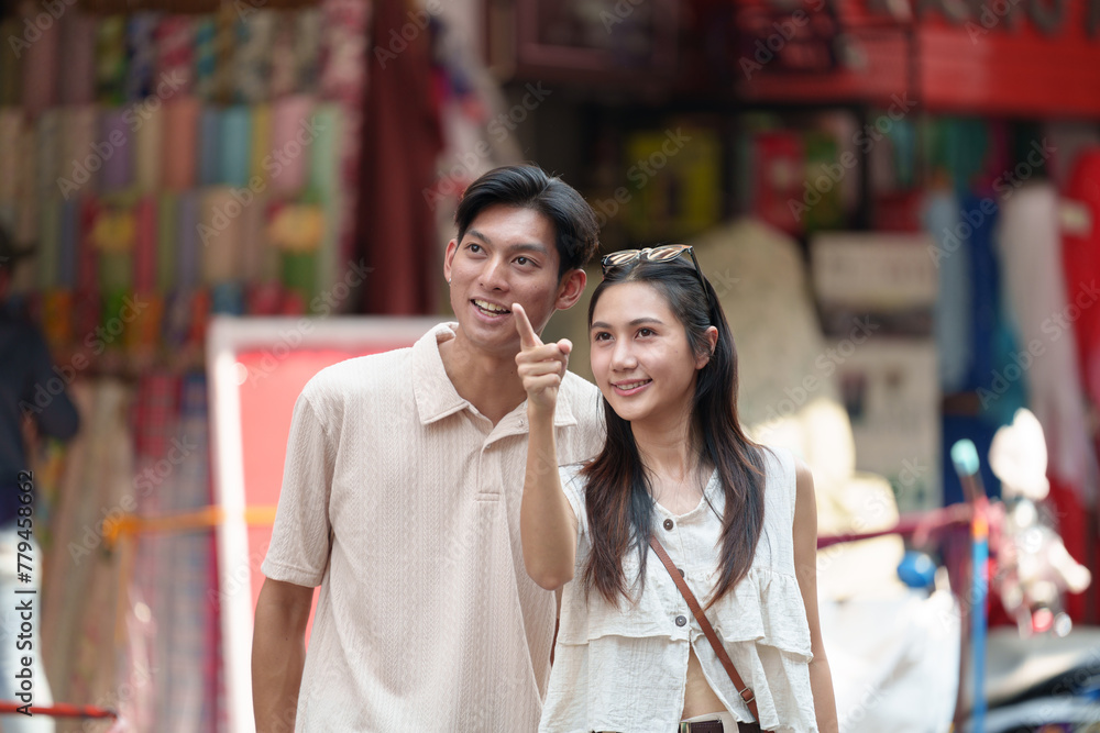 Young Asian tourist couple walking in the tourist city market together. Point your finger at interesting stores for shopping. Traveling people enjoy the concept of native culture. Young Asian tourist couple walking in the tourist city market together. Point your finger at interesting stores for shopping. Traveling people enjoy the concept of native culture.