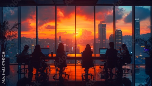 A group of people are seated in front of a large window, gazing out at the city as the sun sets, painting the sky with hues of red and orange in the afterglow of dusk