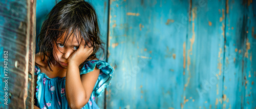 A little offended sad girl stands in front of a solid blue wall and looks directly. Child psychology. Relationship between parents and children. Banner. Copy space photo