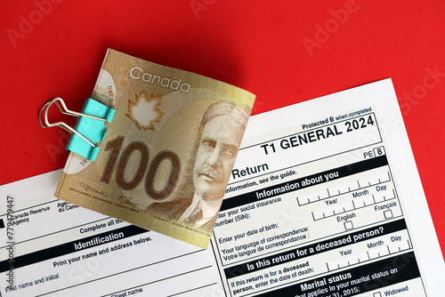 Canadian T1 General tax form Income tax and benefit return lies on table with canadian money bills close up. Taxation and annual accountant paperwork in Canada © mehaniq41