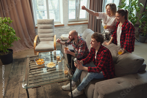 Emotional young people, friends gathering in living room at home, eating snacks, drinking beer and watching online football match translation. Concept of sport, championship, leisure and entertainment photo