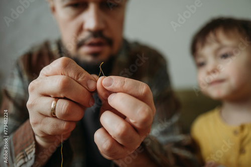 Boy with father trying to put thread in needle at home photo
