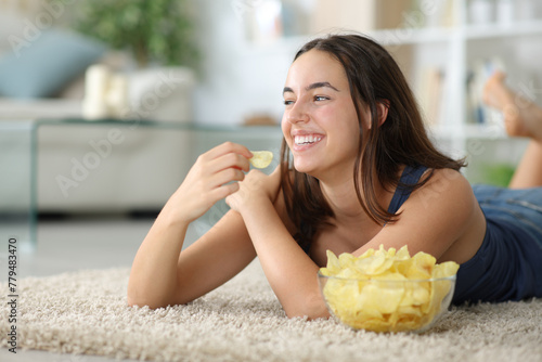 Happy woman eating potato chips on a carpet at home