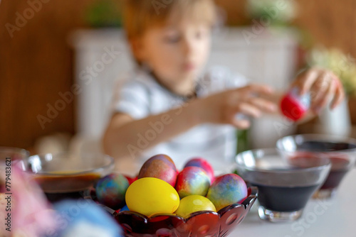 Beatiful blond child  boy  coloring and painting eggs for Easter at home