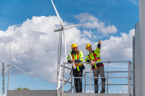 Two workers on a platform looking at a wind turbine
