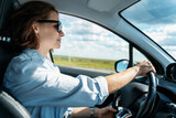Young Caucasian woman in sunglasses driving a car in the countryside on a summer day