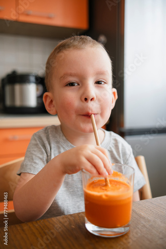 Boy drinking apple carrot juice through straw at home