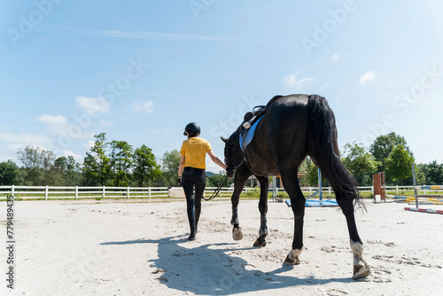 Instructor walking with black horse at manege square